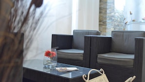 A modern hotel lobby with grey upholstered seating, a glass table with a vase of red flowers, and a stone accent wall. - La Villa (Montagnana)
