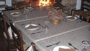 Un comedor con chimenea de piedra, una mesa dispuesta para cuatro personas y un jarrón con flores secas en la repisa.