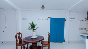 Un comedor con una mesa redonda de madera, dos sillas, una planta en maceta y una cortina azul.