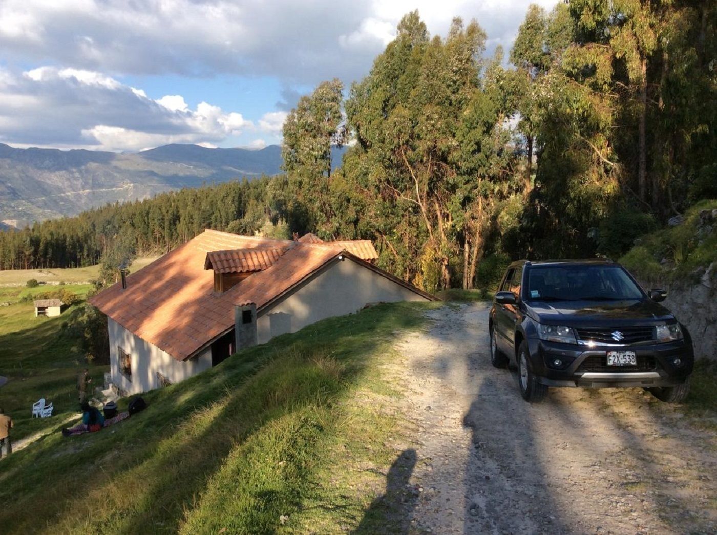 A rustic house with a dirt road leading to it, surrounded by trees and mountains.