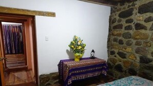 Une pièce avec une porte en bois, une petite table recouverte d’une nappe à motifs, un vase rempli de fleurs et un lit agrémenté d’une couvre-lit à motifs.