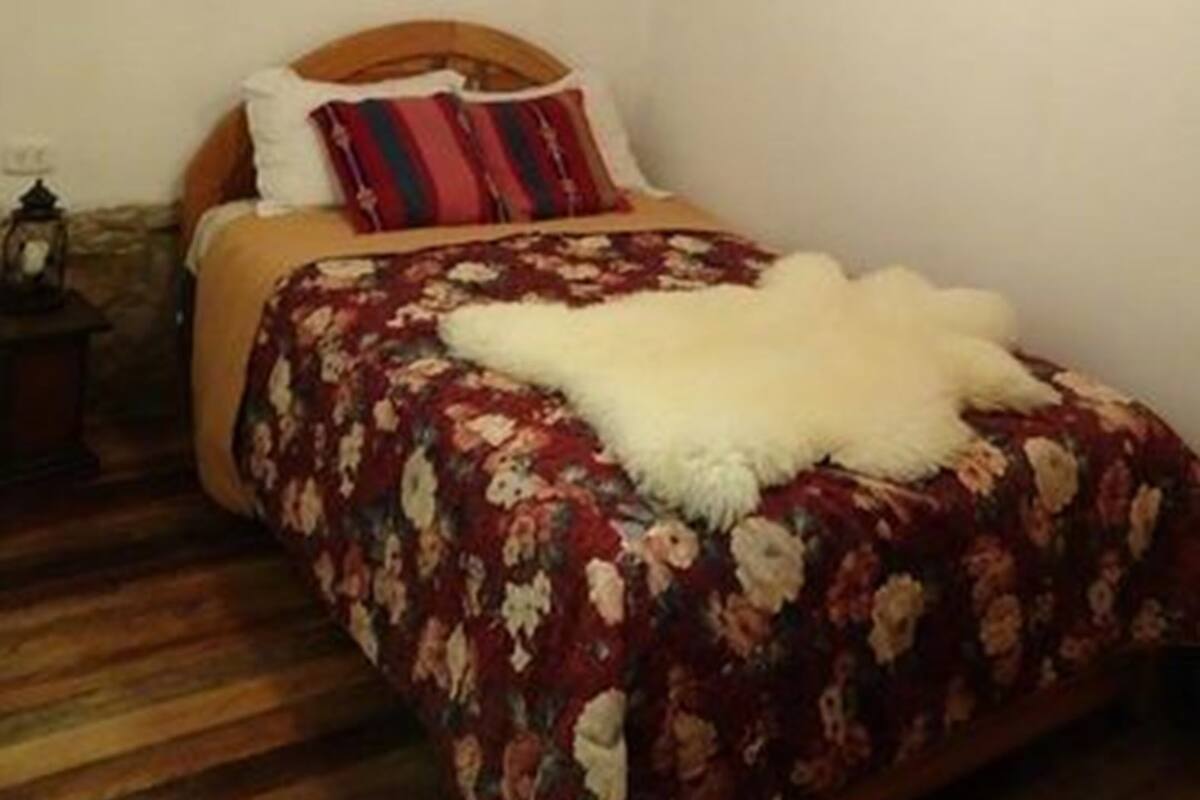 A bedroom with a wooden ceiling, a bed with floral bedding, and a white fluffy throw.