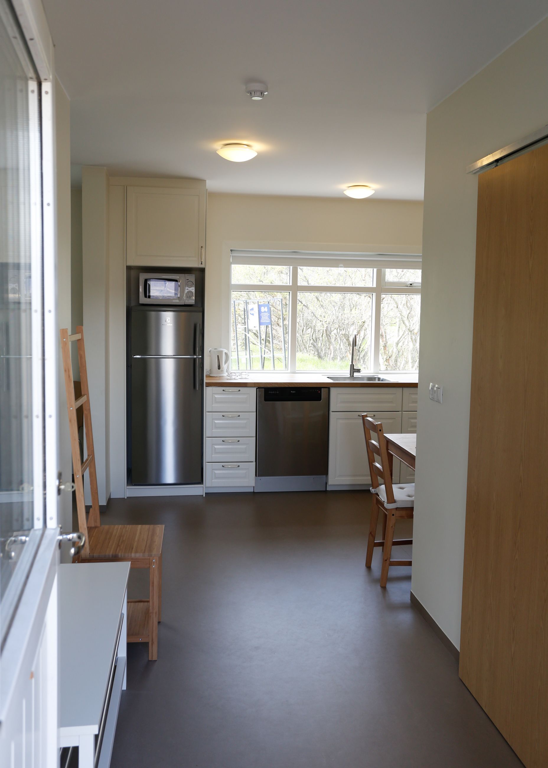 Una cocina moderna con refrigerador, microondas, lavavajillas y ventana con vista a árboles.