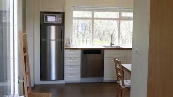 Una cocina moderna con refrigerador, microondas, lavavajillas y ventana con vista a árboles.