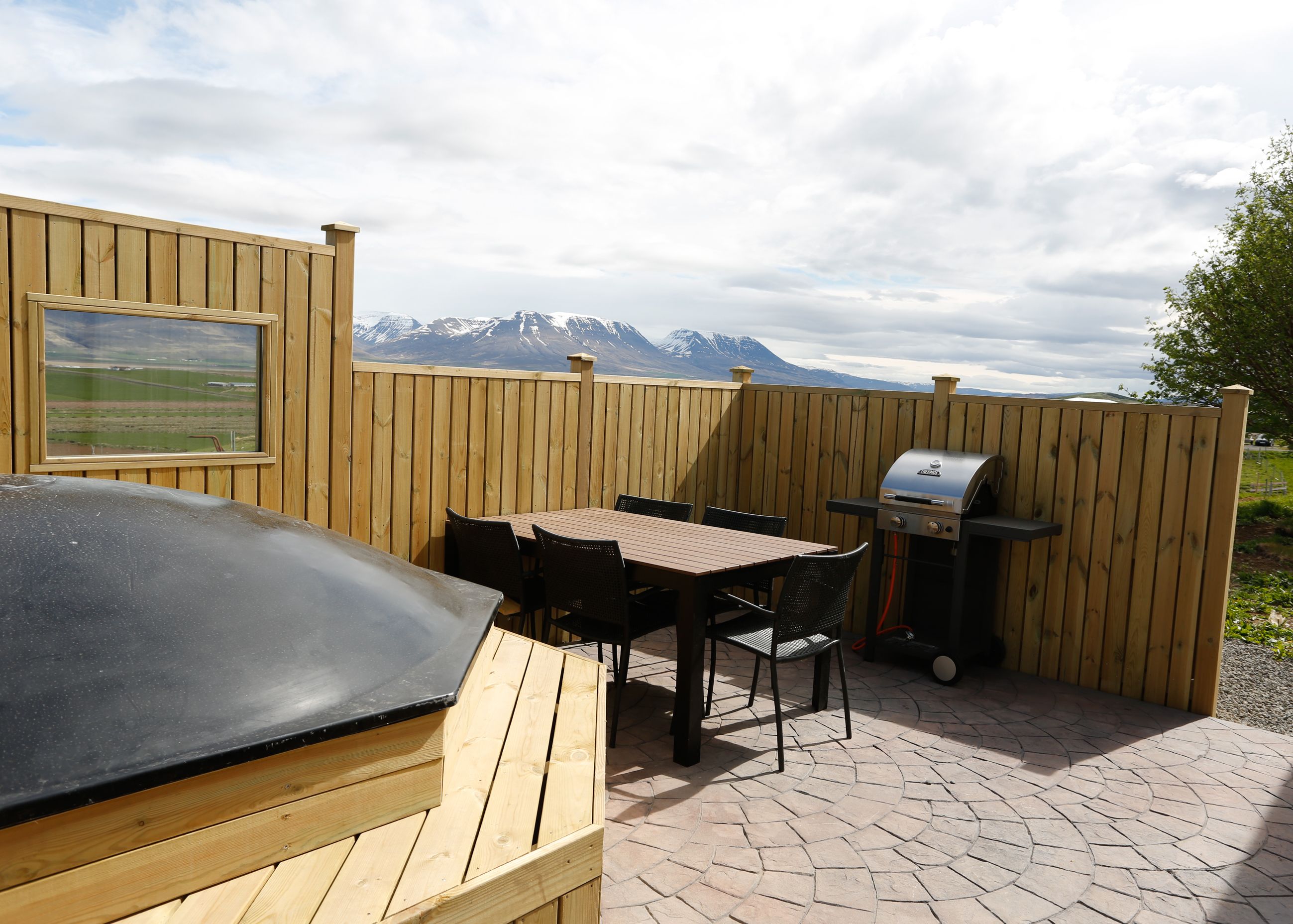 Eine Terrasse im Freien mit Holztisch und -stühlen, einem Grill und Blick auf schneebedeckte Berge.