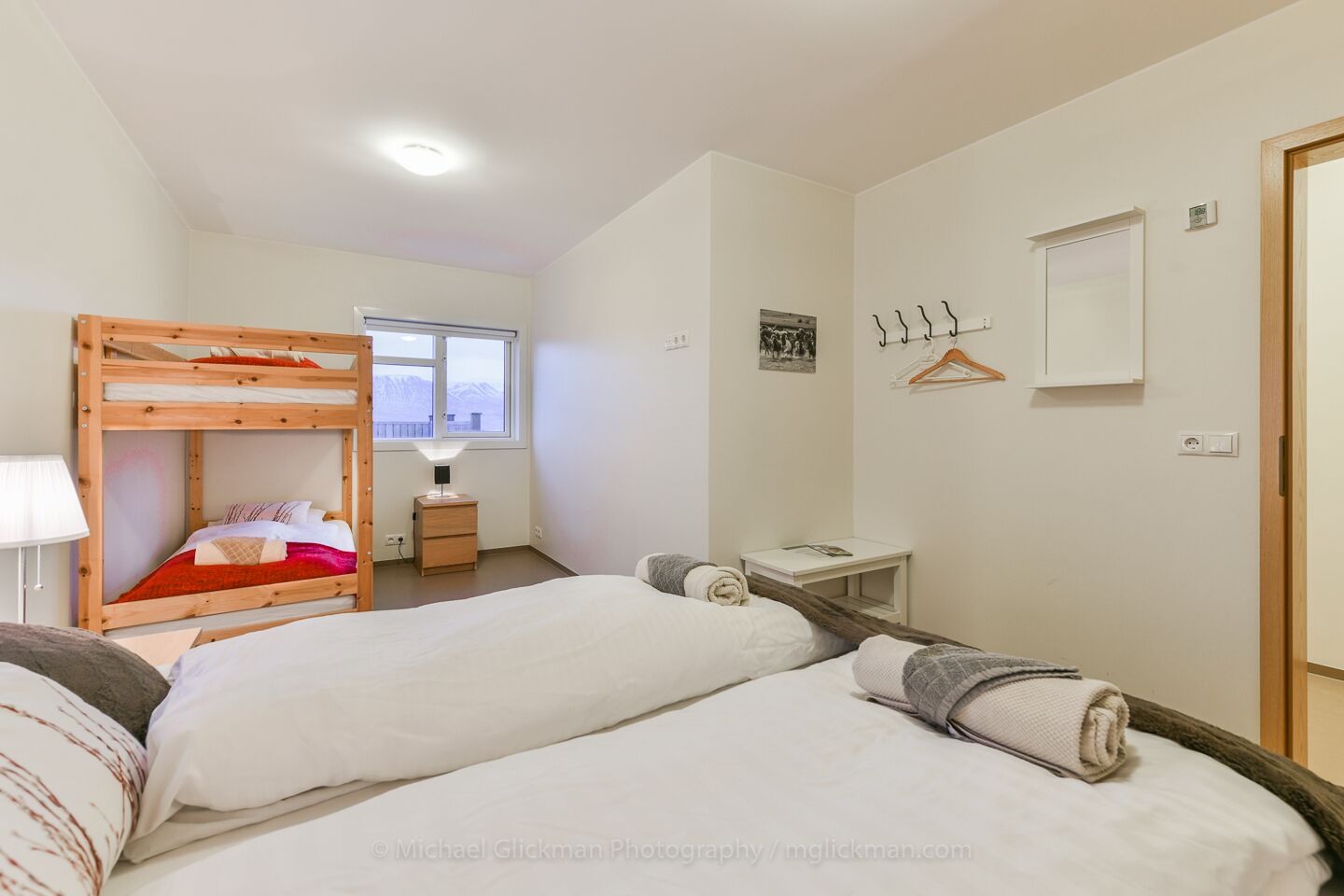 Un dormitorio con literas, una mesita de noche, una lámpara, un escritorio pequeño, un espejo y una ventana con vistas a montañas.