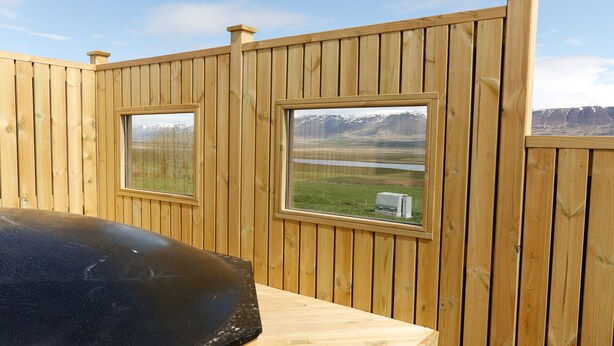 Eine Holzterrasse mit zwei Fenstern und Blick auf eine gebirgige Landschaft.