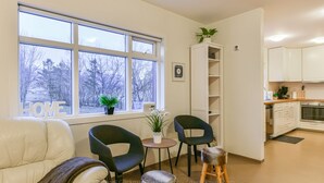 Ein modernes Wohnzimmer mit einer Couch, zwei Sesseln, einem kleinen Tisch und einem Fenster mit Blick auf Bäume.