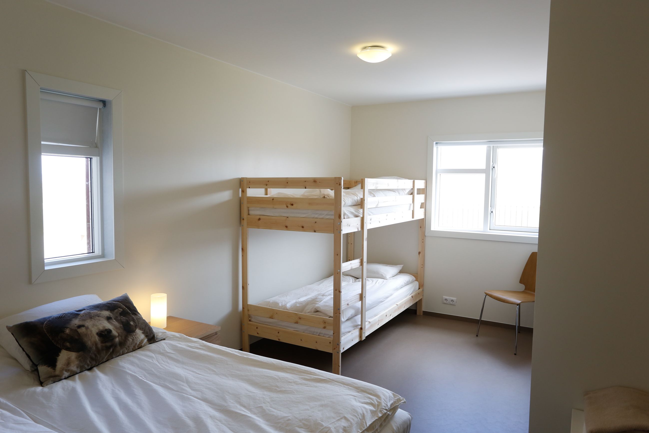 Een kamer met stapelbedden, een enkel bed, een stoel en een raam.