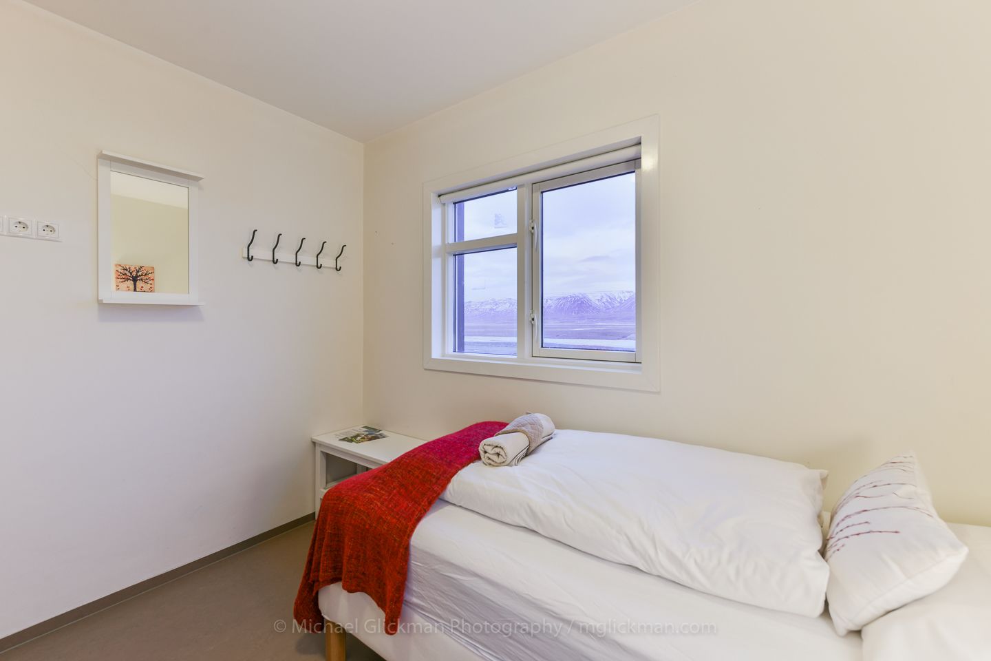 Une chambre à coucher avec un lit, une fenêtre donnant sur un beau paysage, une table de chevet et un miroir fixé au mur.