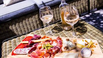 Een rieten tafeltje met een charcuterieplank, twee wijnglazen en een fles wijn.