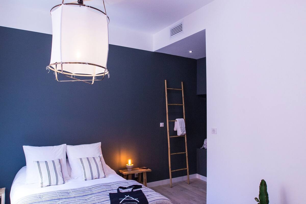 A modern bedroom with a bed, bedside table, lamp, ladder, and a potted plant.