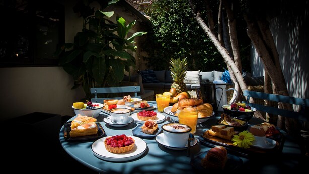An outdoor dining table with a variety of breakfast items including pastries, fruits, and beverages. - Antichambre (Nîmes)