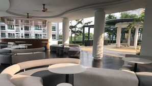 Un área de descanso moderna con sofás, mesas redondas y vistas a un edificio con balcones.