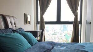 Un dormitorio con un ventanal grande, una cama con muchas almohadas, un escritorio y una silla.