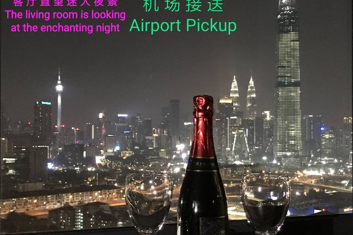 A night view of a city skyline with illuminated buildings, a bottle, and two glasses on a table.