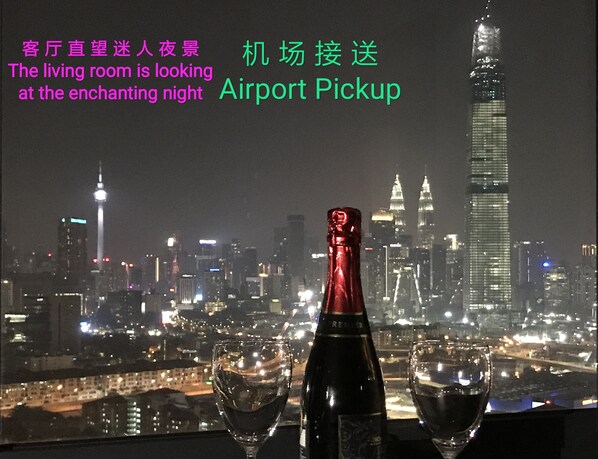A night view of a city skyline with illuminated buildings, a bottle, and two glasses on a table.