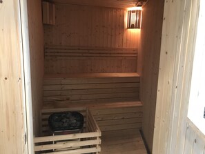 A wooden sauna with a bench and a container of stones.