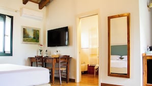 Una habitación de hotel con cama, un escritorio con silla, televisor, un cuadro y un espejo grande.