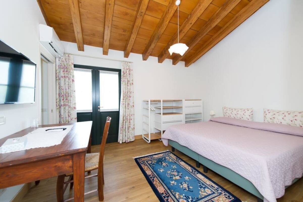 Un dormitorio con techo de madera, una cama con edredón estampado de flores, un escritorio con silla y una ventana con cortinas.