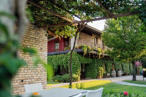 A brick building with a red door, a balcony with plants, and a garden area with tables and chairs. - Alloggio Agrituristico Albafiorita (Latisana)