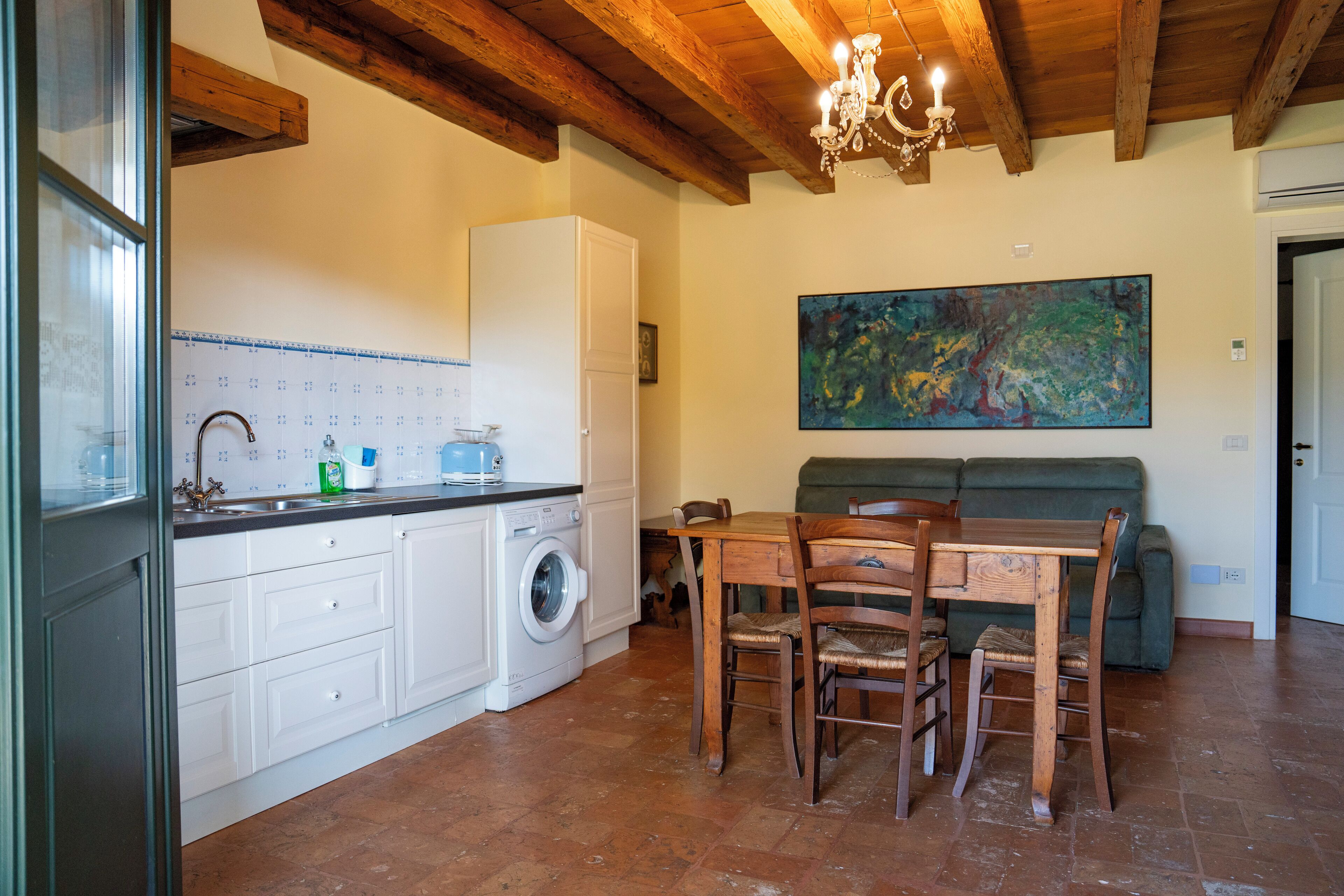 Une cuisine avec des meubles blancs, un lave-linge et un coin repas comprenant une table et des chaises.
