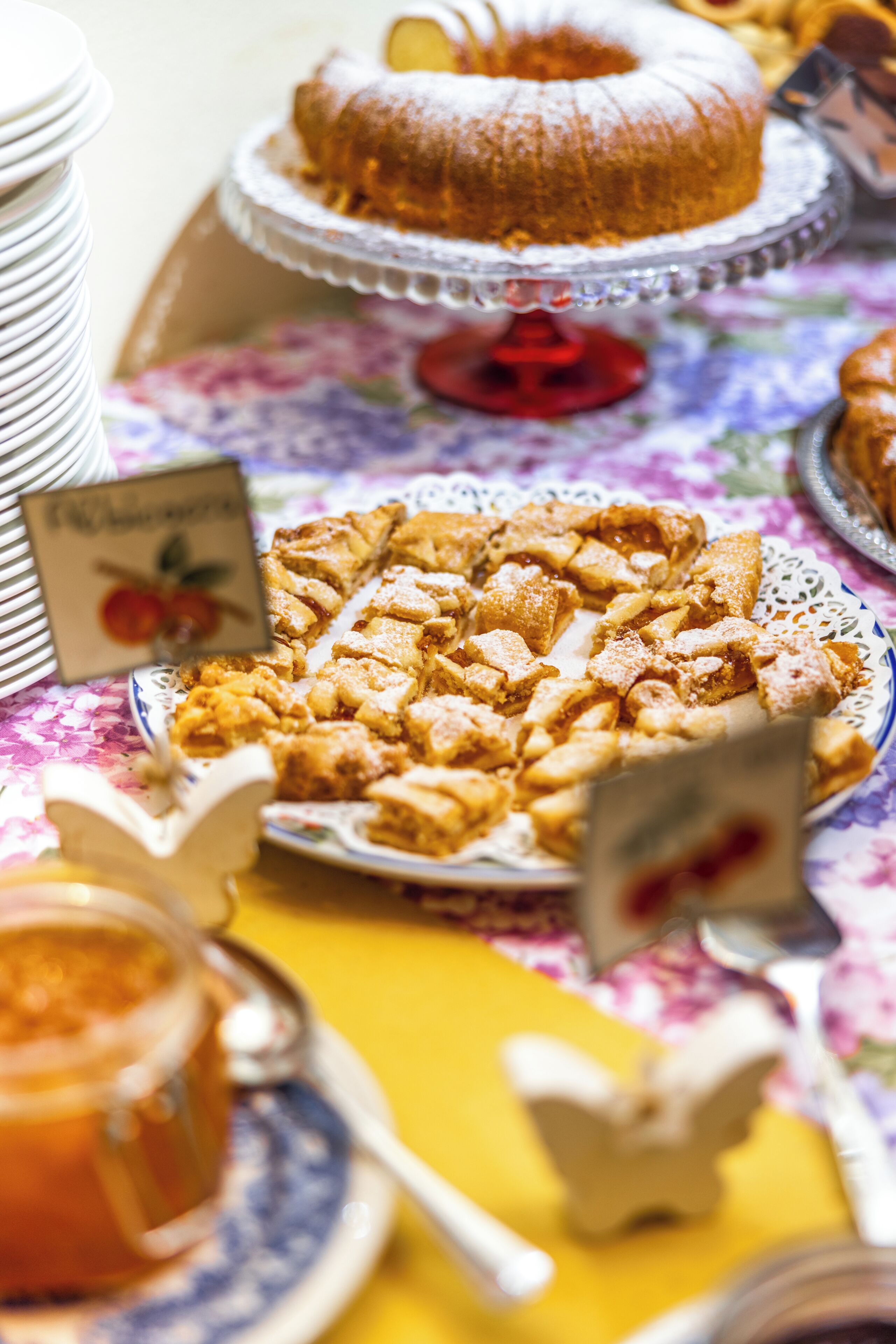 A table with a variety of desserts, including a bundt cake and a lattice-topped pie, on a floral tablecloth.