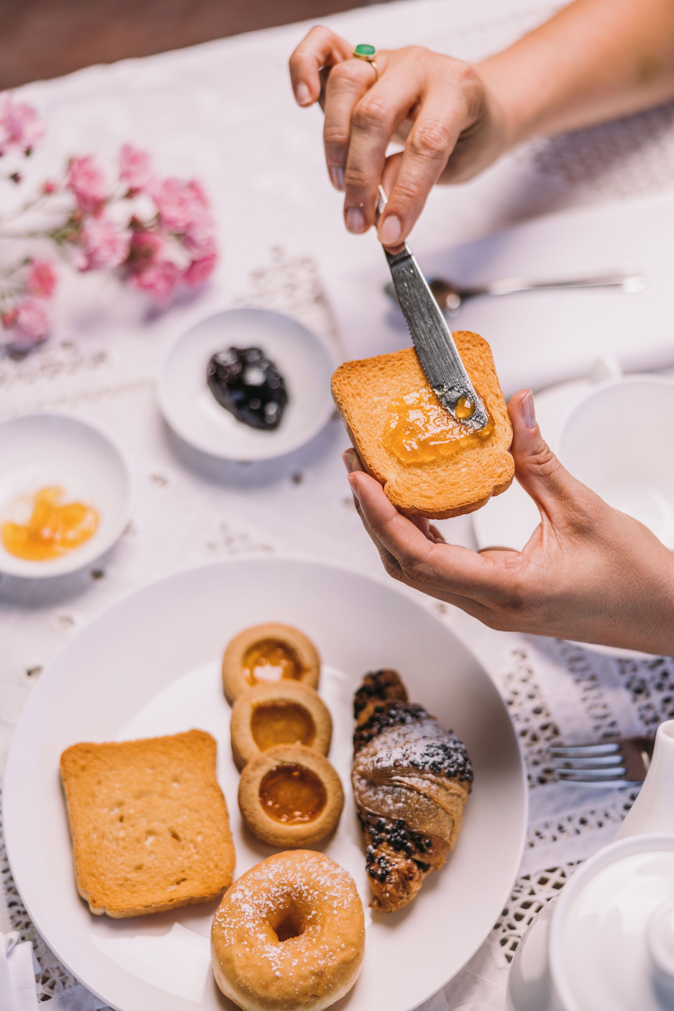 A person spreading butter on toast, with a plate of pastries and a teapot on a table.