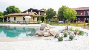 Una piscina con borde de piedra, cerca de madera y un edificio con tejado de baldosas.