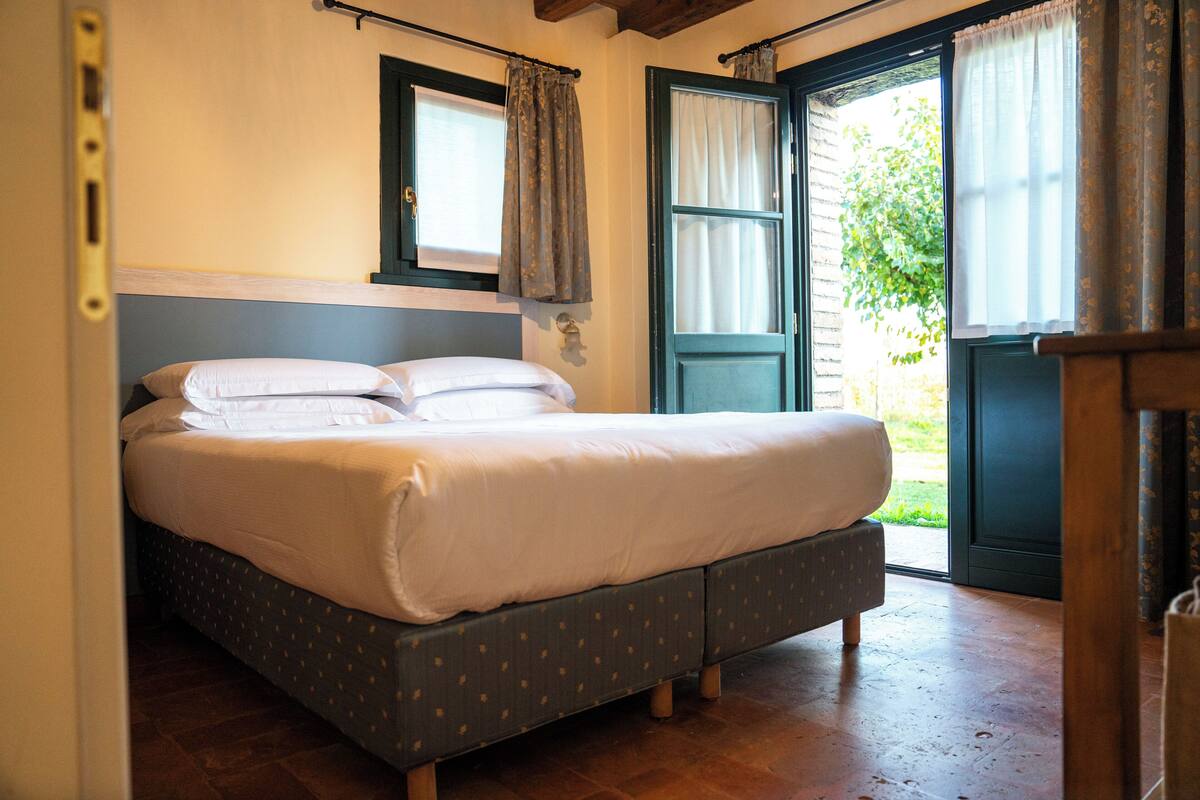 Una cama doble con cabecera de madera, una ventana con cortinas y una puerta que da al exterior.