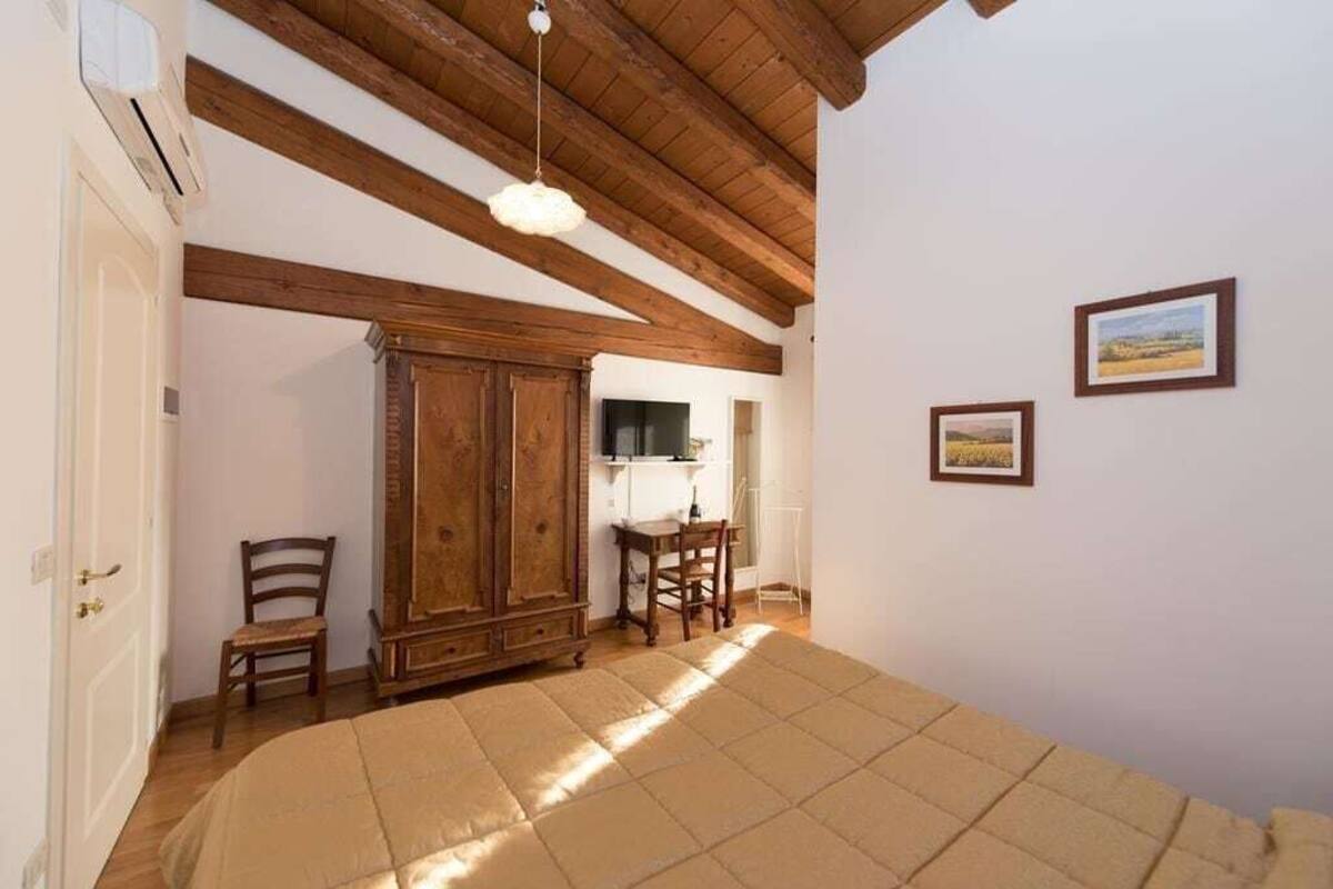 Un dormitorio con una cama grande, vigas de madera en el techo, un armario y dos cuadros en la pared.