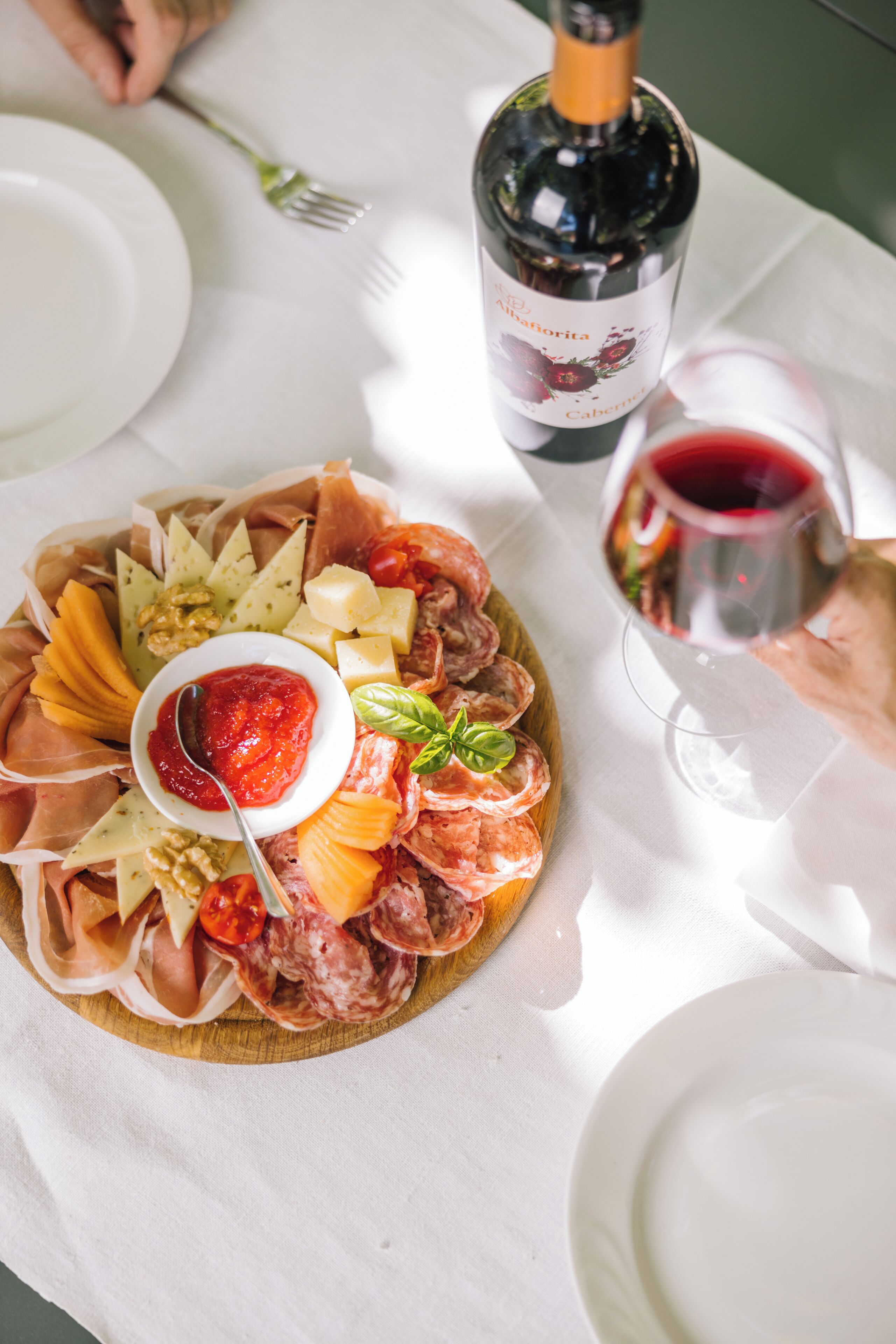 Una tabla de embutidos con varios tipos de carne, quesos y una botella de vino sobre una mesa.
