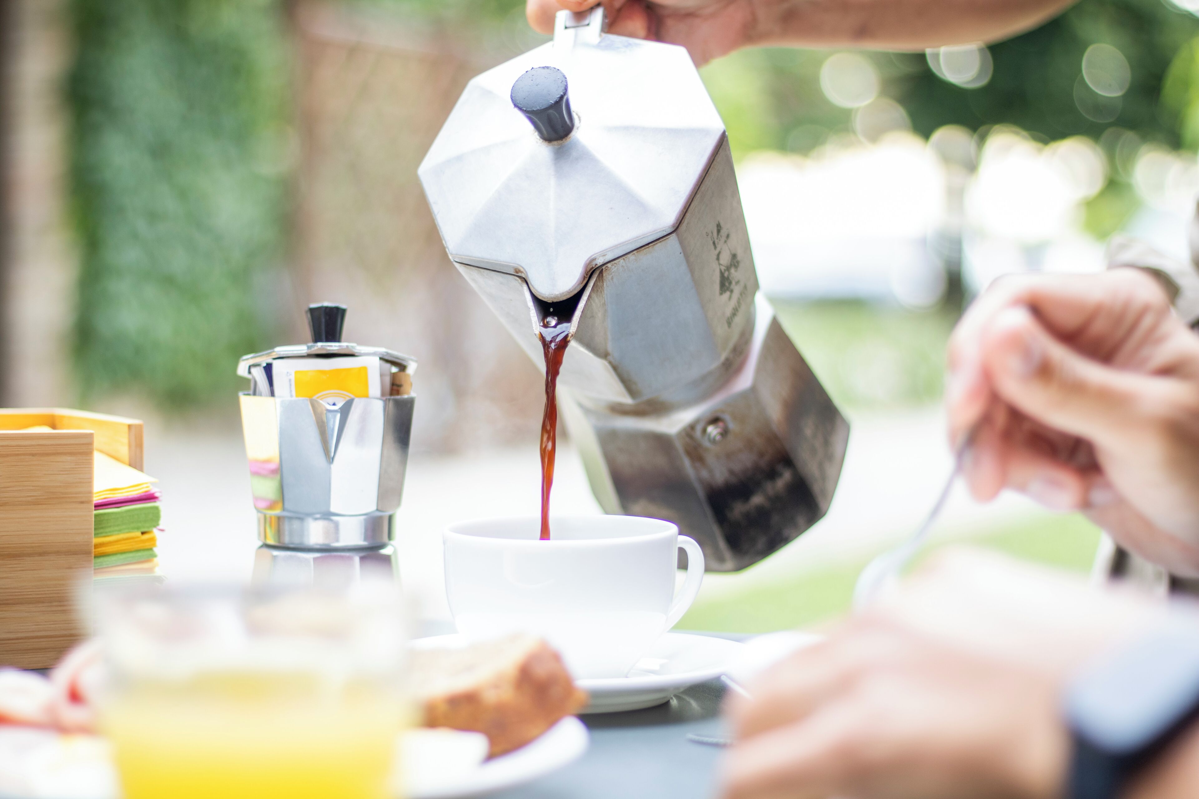 Una máquina de café sirviendo café en una taza, una pila de libros y una rebanada de tostada sobre una mesa.