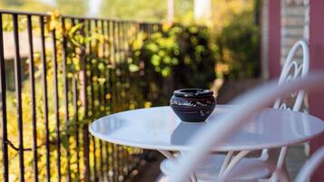 A white metal table with a ceramic bowl on it, set on a balcony with a metal railing and greenery in the background.