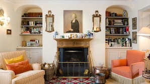 A cozy living room with a fireplace, striped armchairs, and a bookshelf filled with books and decorative items. - Heron House (Tiverton)