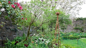 A garden with a variety of flowers, a tall plant structure, and a stone wall. - Heron House (Tiverton)