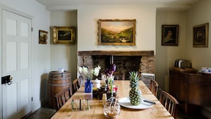 A dining room with a wooden table set for four, a stone fireplace, and framed artwork on the walls. - Heron House (Tiverton)
