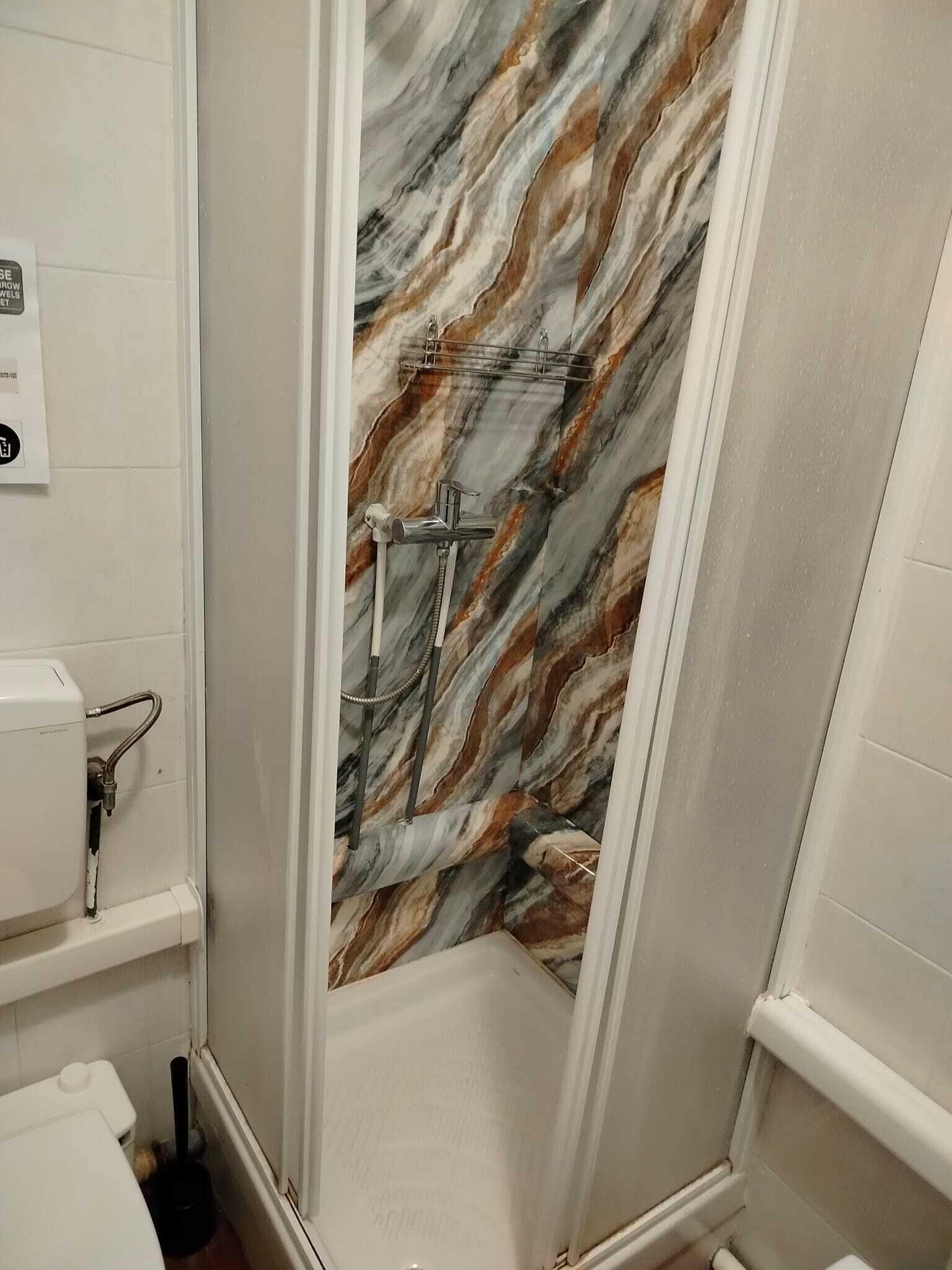 A bathroom with a marble wall, a shower, and a toilet.