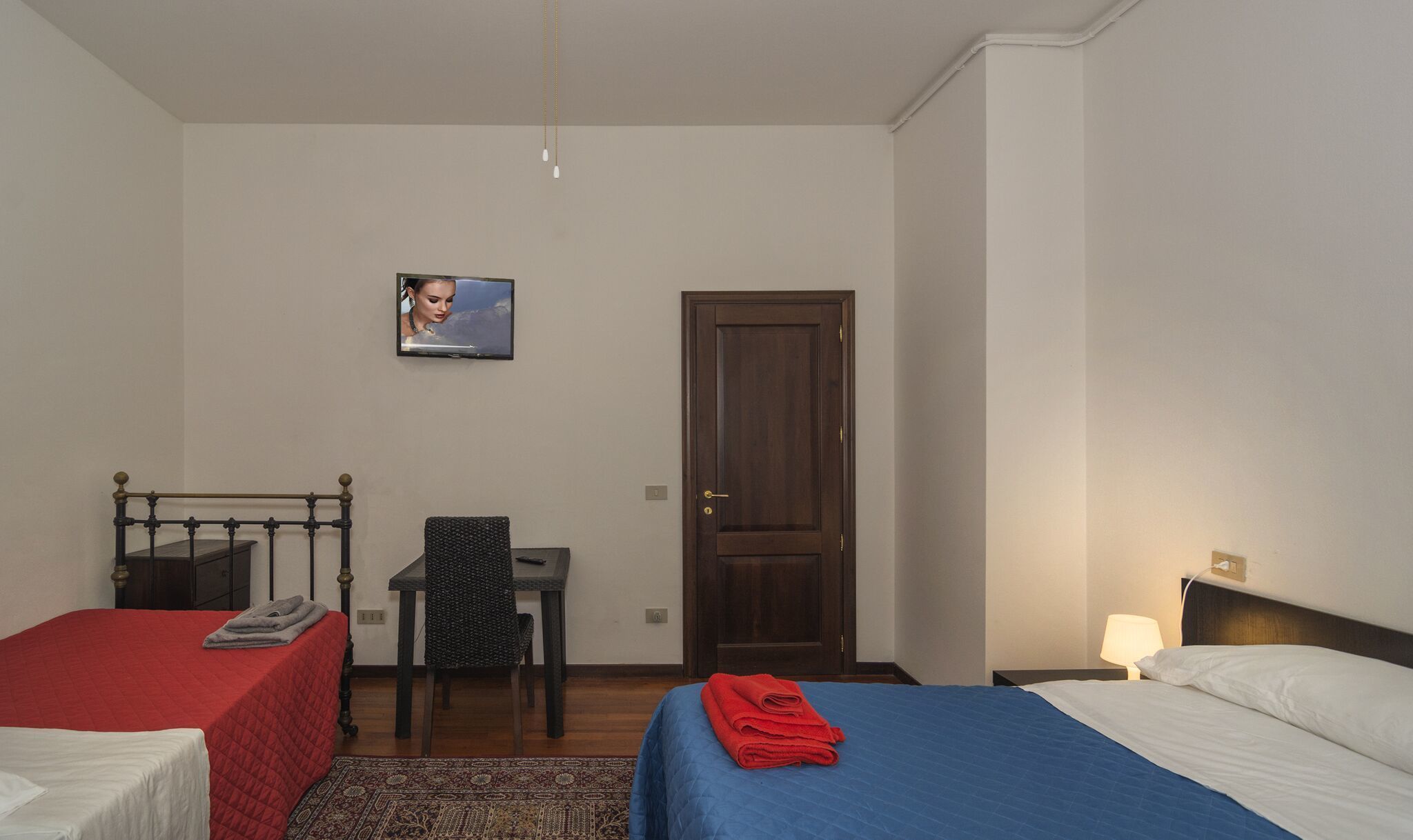 A hotel room with two beds, a desk, a chair, a television, and a door.