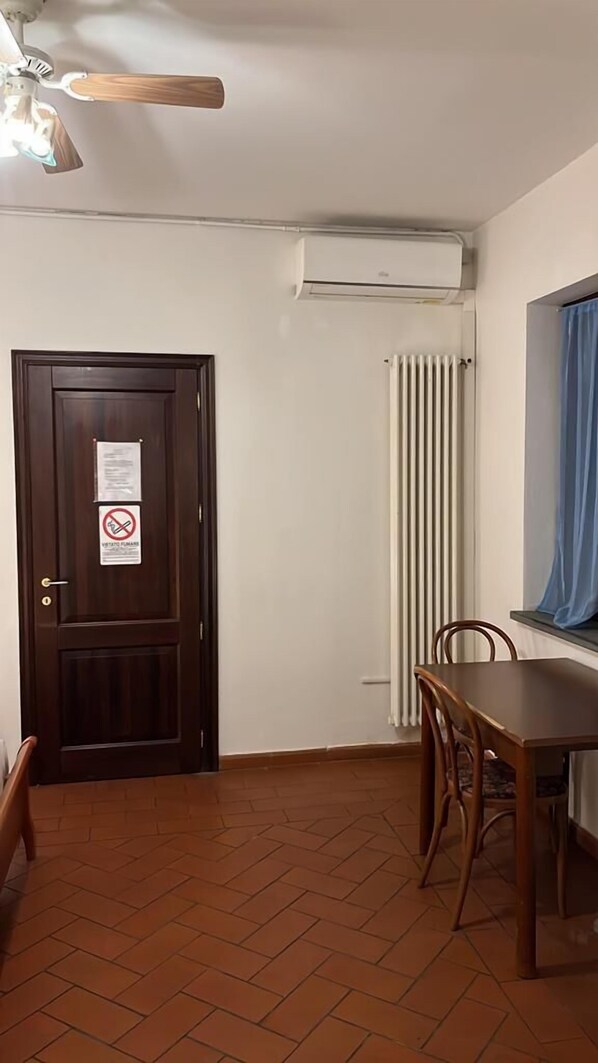A room with a wooden door, a radiator, a ceiling fan, and a dining table with chairs. - Il Cielo di Lucio (Pisa)