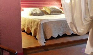 A bed with a quilted bedspread and pillows, a wooden bench, and a striped wall. - La Chamberte (Villeneuve-les-Beziers)