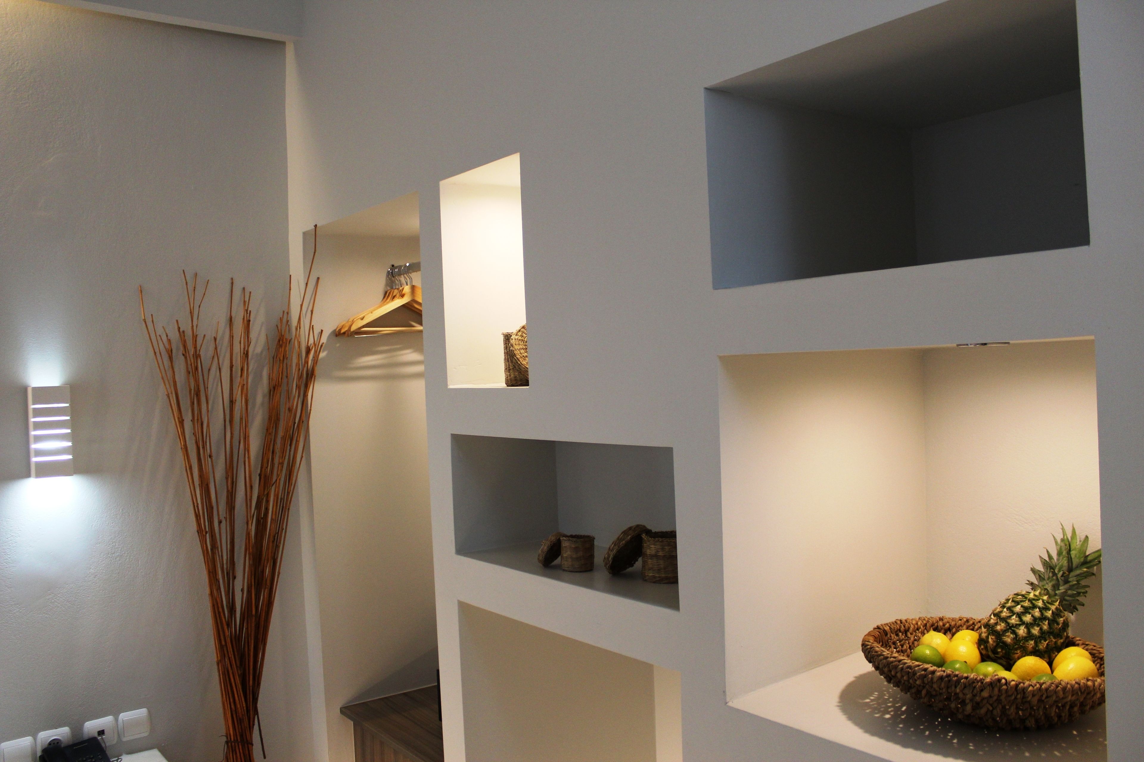 A room with a white wall, a shelf with decorative items, and a basket of fruit.