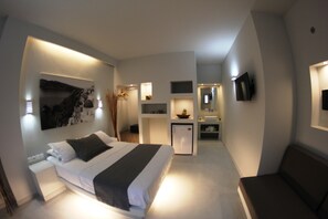 Et moderne hotelværelse med seng, et lille tekøkken, et siddeområde og et fjernsyn ophængt på væggen.
