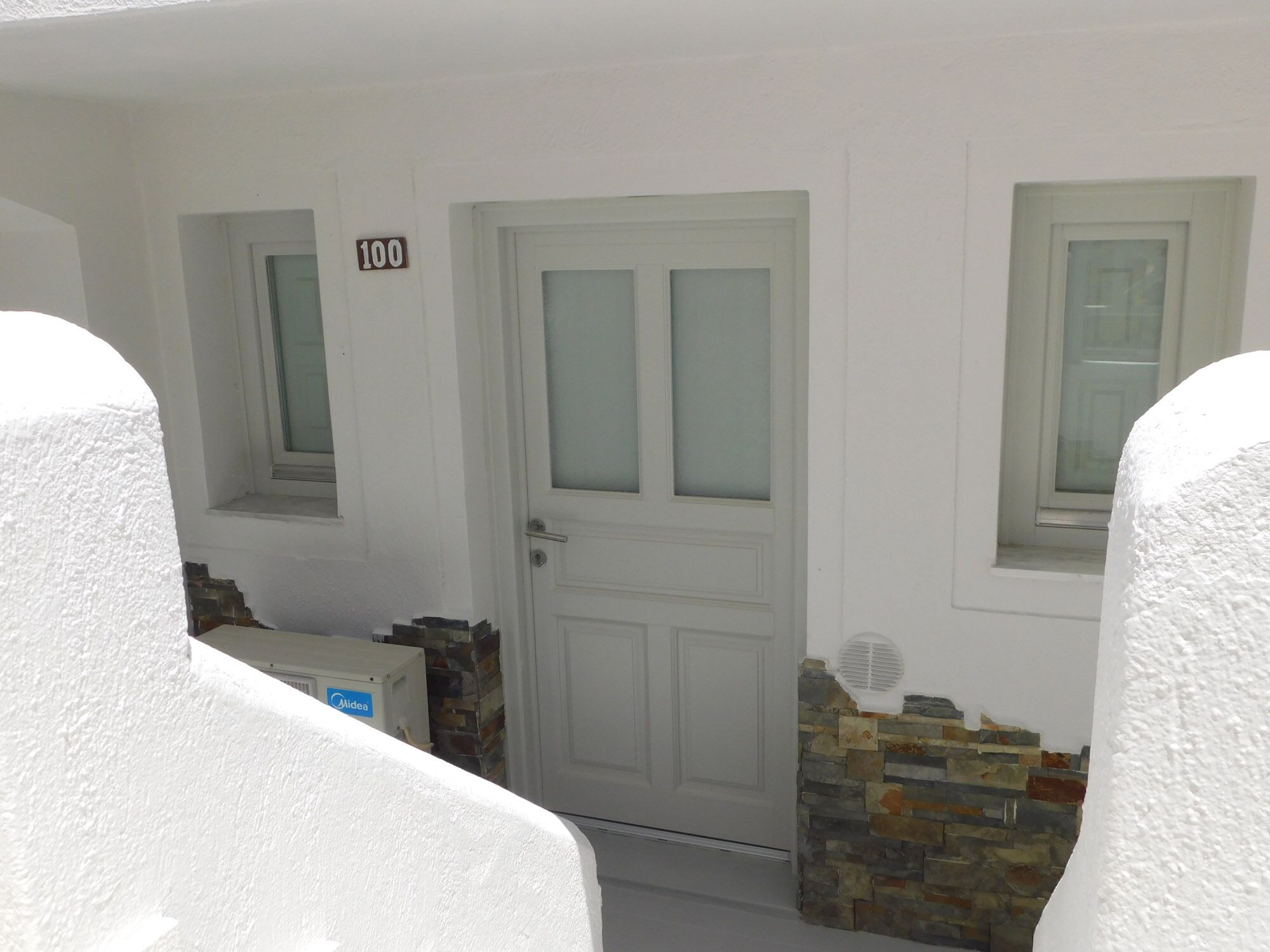 A white door with frosted glass panels, a stone wall, and a small window with a shutter.
