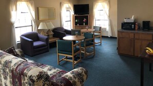 A living room with a sofa, chairs, a table, a ceiling fan, a TV, and a kitchen area with a microwave and coffee maker. - Rest Inn Motel (Palestine)