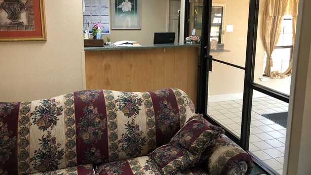 A reception area with a wooden desk, a laptop, and a framed picture on the wall. - Rest Inn Motel (Palestine)