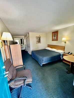 A hotel room with a bed, desk, chair, and a small table.