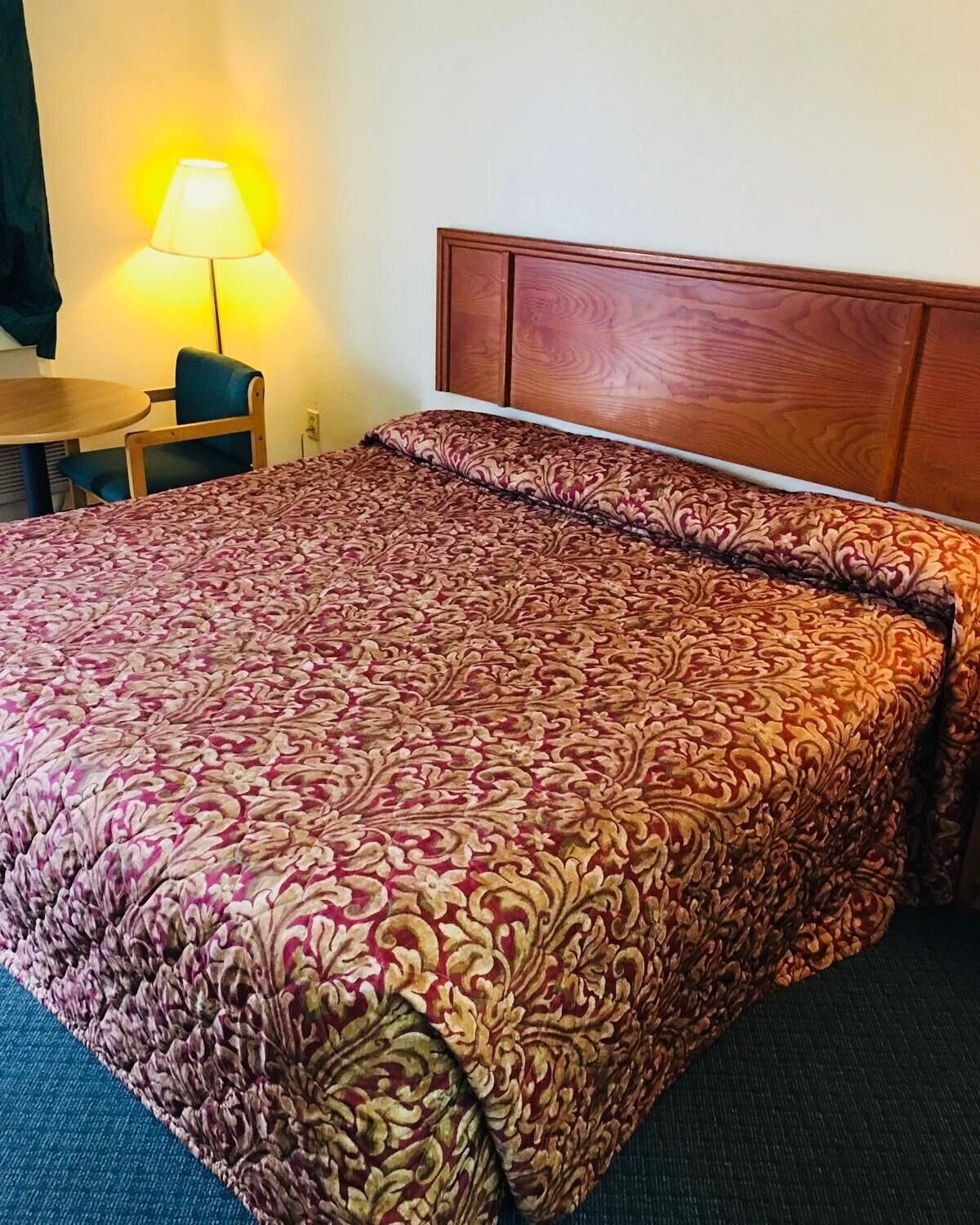 A hotel room with a large bed, a wooden headboard, a bedside table, and a lamp.
