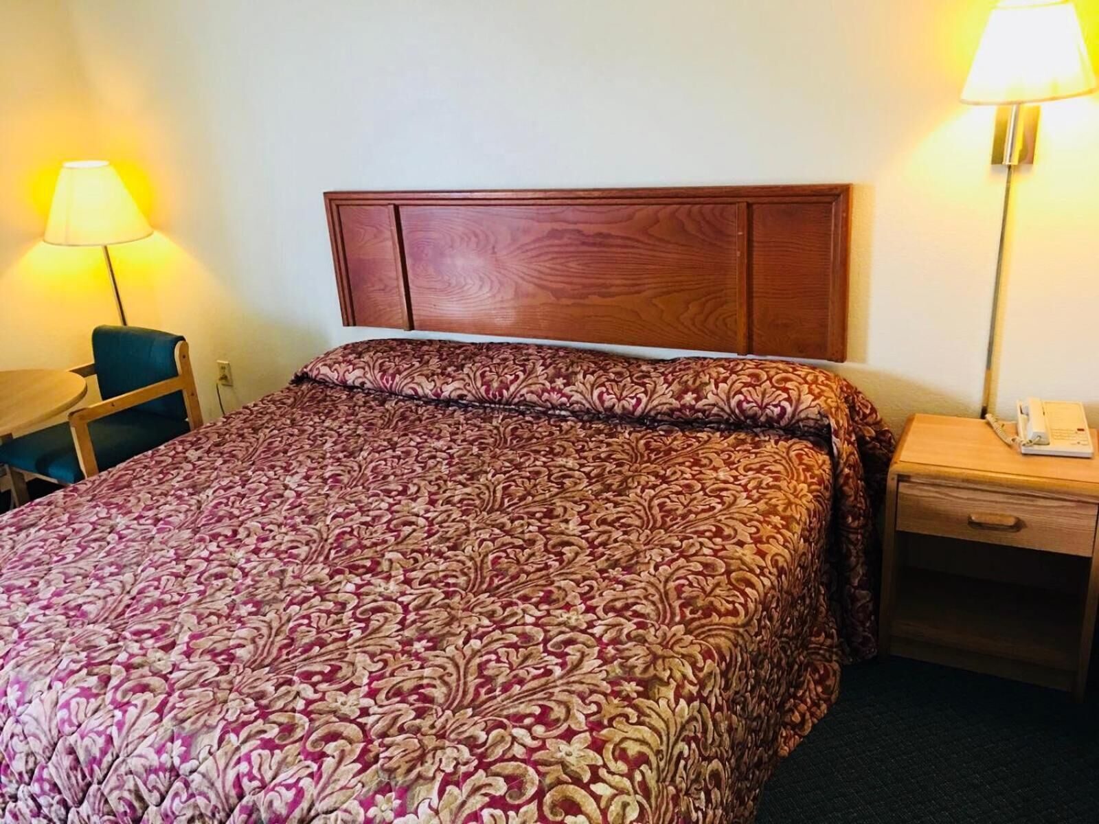 Een hotelkamer met een groot bed, een houten hoofdbord, een bureau met stoel en een nachtkastje met lamp en telefoon.