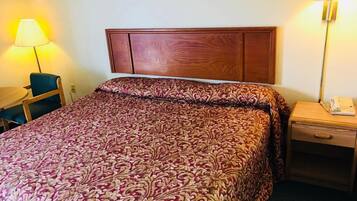 Een hotelkamer met een groot bed, een houten hoofdbord, een bureau met stoel en een nachtkastje met lamp en telefoon.